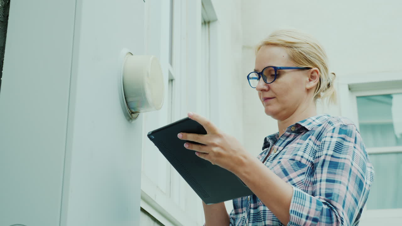 A Woman Records The Readings Of A Counter Mounted On The Wall Of A House Uses A Tablet