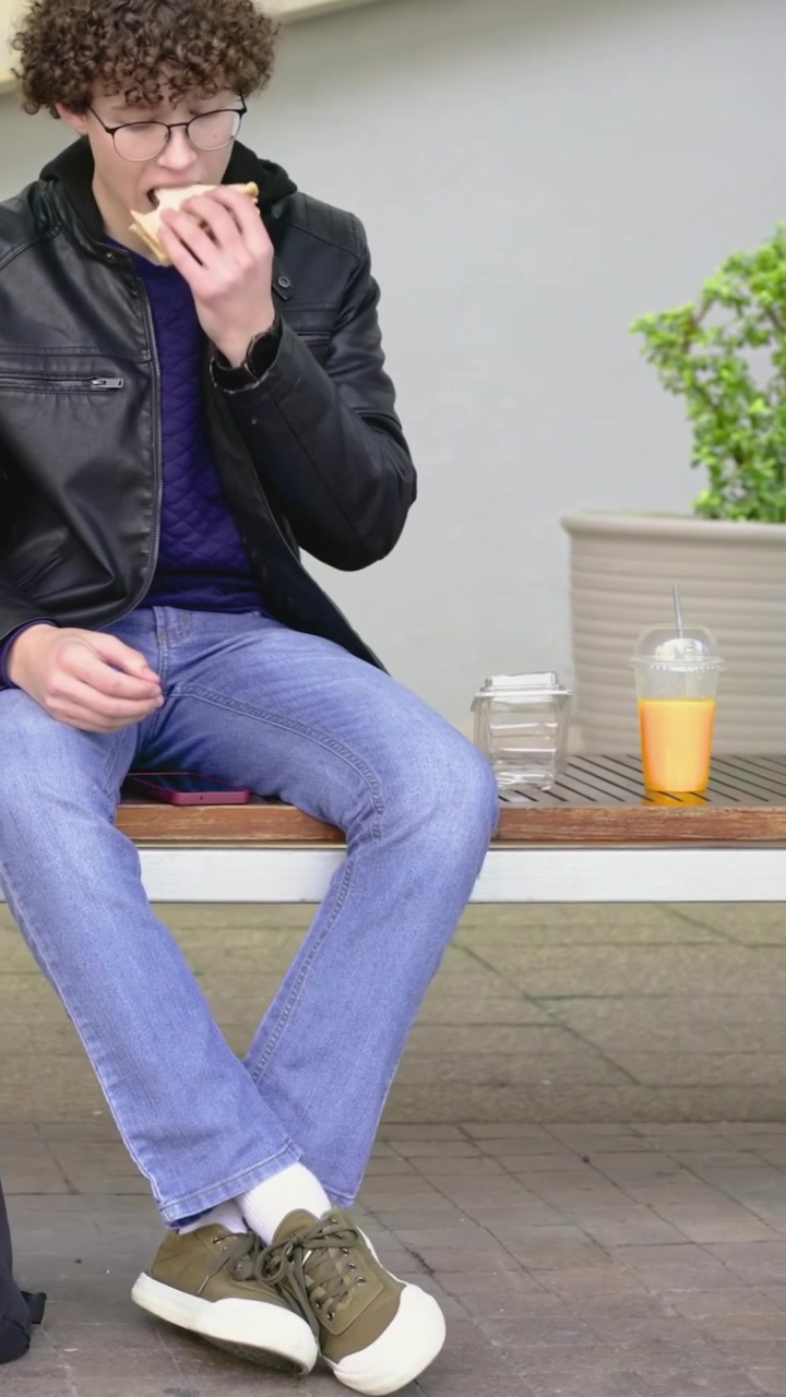 Vertical video: Sitting man in coat sipping eating sandwich on seat placing cup leaving, copy space