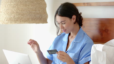 Woman in pajamas using laptop in bed, smiling and enjoying morning routine, at home