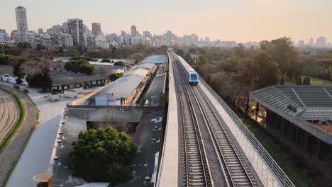 vista aérea da passagem do trem da linha mitra com o horizonte de buenos aires ao fundo durante o pôr do sol