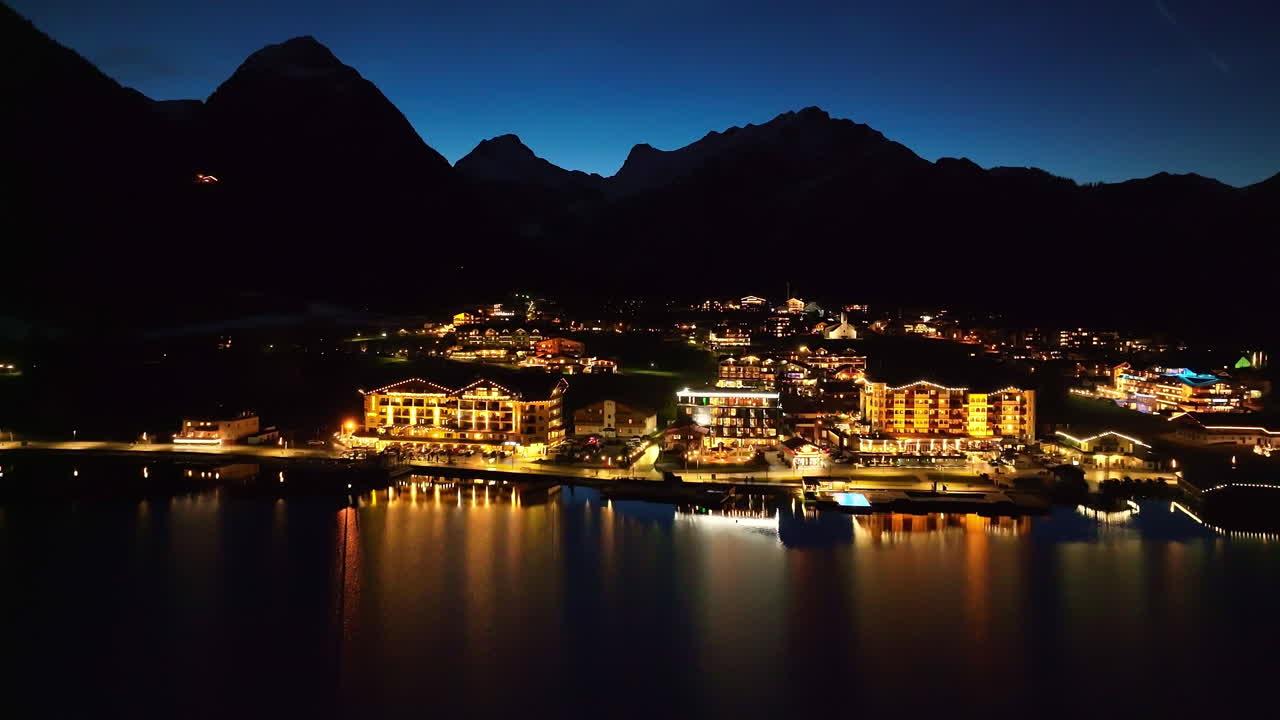 오스트리아의 티롤 지역에 있는 아첸제 호수에서 밤에 조명이 켜진 페르티사우 마을의 공중 전망 - 드론 샷