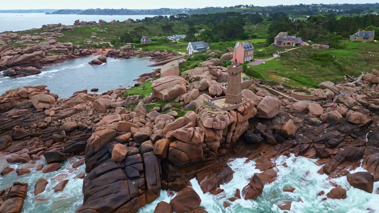 Mean Ruz lighthouse in Ploumanac'h, pink granite boulders, waves crash on rugged coast of Brittany, France. Aerial backward