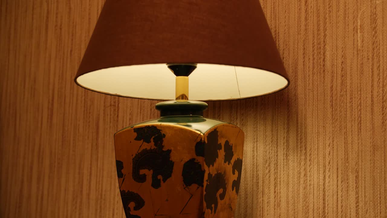 Pan shot of a patterned vintage lamp with a warm glowing shade