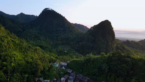 Aerial-flyover-small-village-located-between-green-hills-during-sunny-day-in-Indonesia