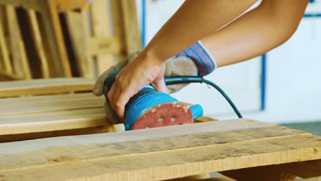 A-Young-Woman-Holding-Firmly-The-Grinder-While-Polishing-The-Edges-Of-A-Wooden-Pallet---Close-Up-Shot