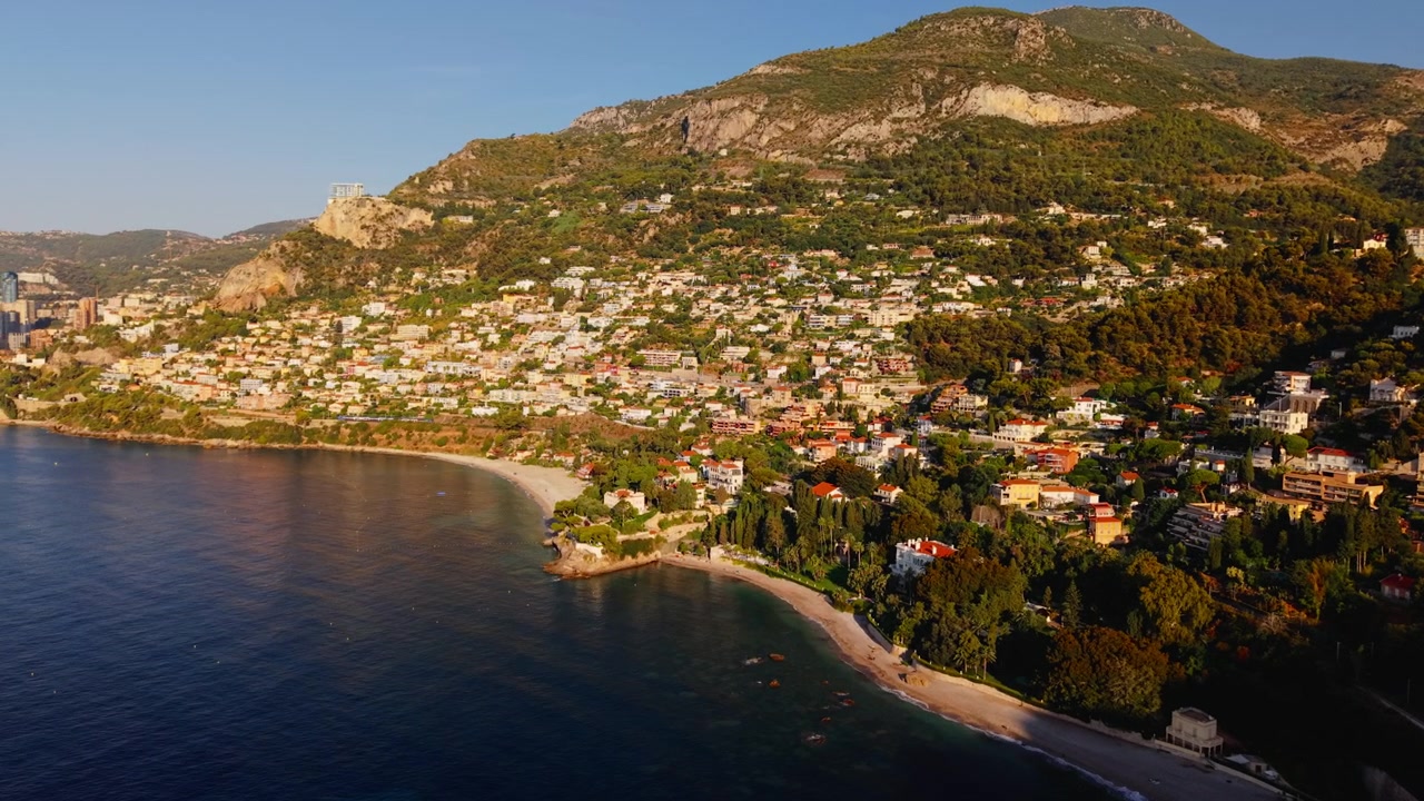 Vista aérea da costa de Monte Carlo e casas na encosta ao pôr do sol, cenário mediterrâneo.