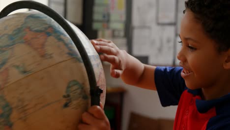 vista lateral de un escolar afroamericano estudiando el globo en el escritorio en el aula de la escuela 4k