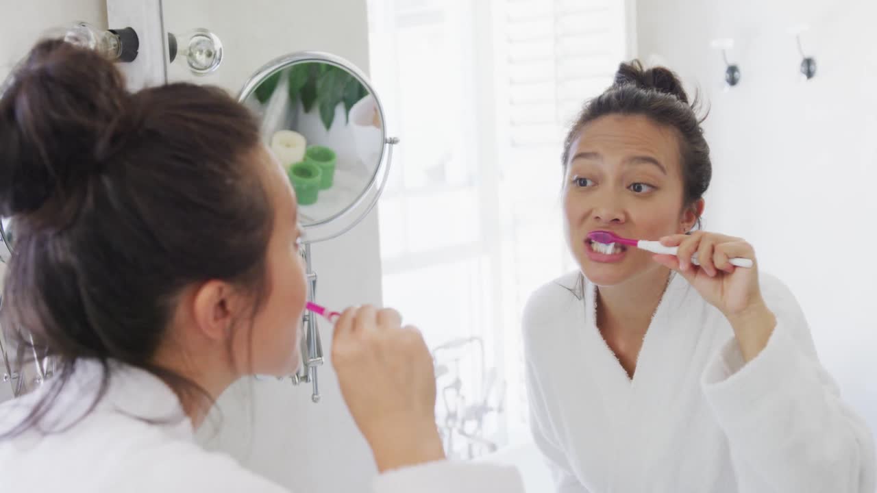 Happy asian woman looking at mirror and brushing teeth in bathroom, in slow motion