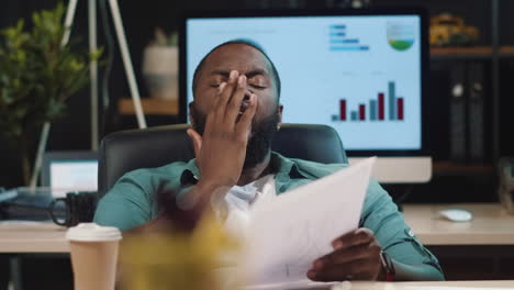 Closeup-exhausted-afro-business-man-looking-at-papers-in-hipster-office.