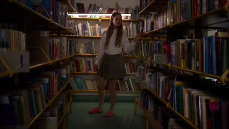 schoolgirl enjoying the school library, walking among bookshelves, handheld shot