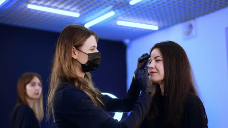female beauty specialist wearing mask and latex gloves drawing lines with white pencil. cosmetologist marks the permanent make up zones.