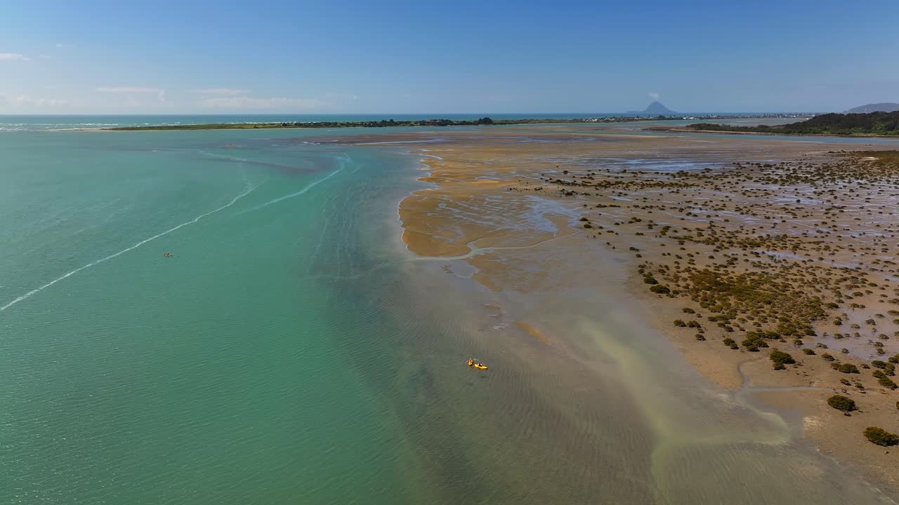 Two kayakers glide through a quiet harbor, oars slicing the glassy water as boats bob nearby and sunlight dances on the gentle ripples around them. New Zealand hobby