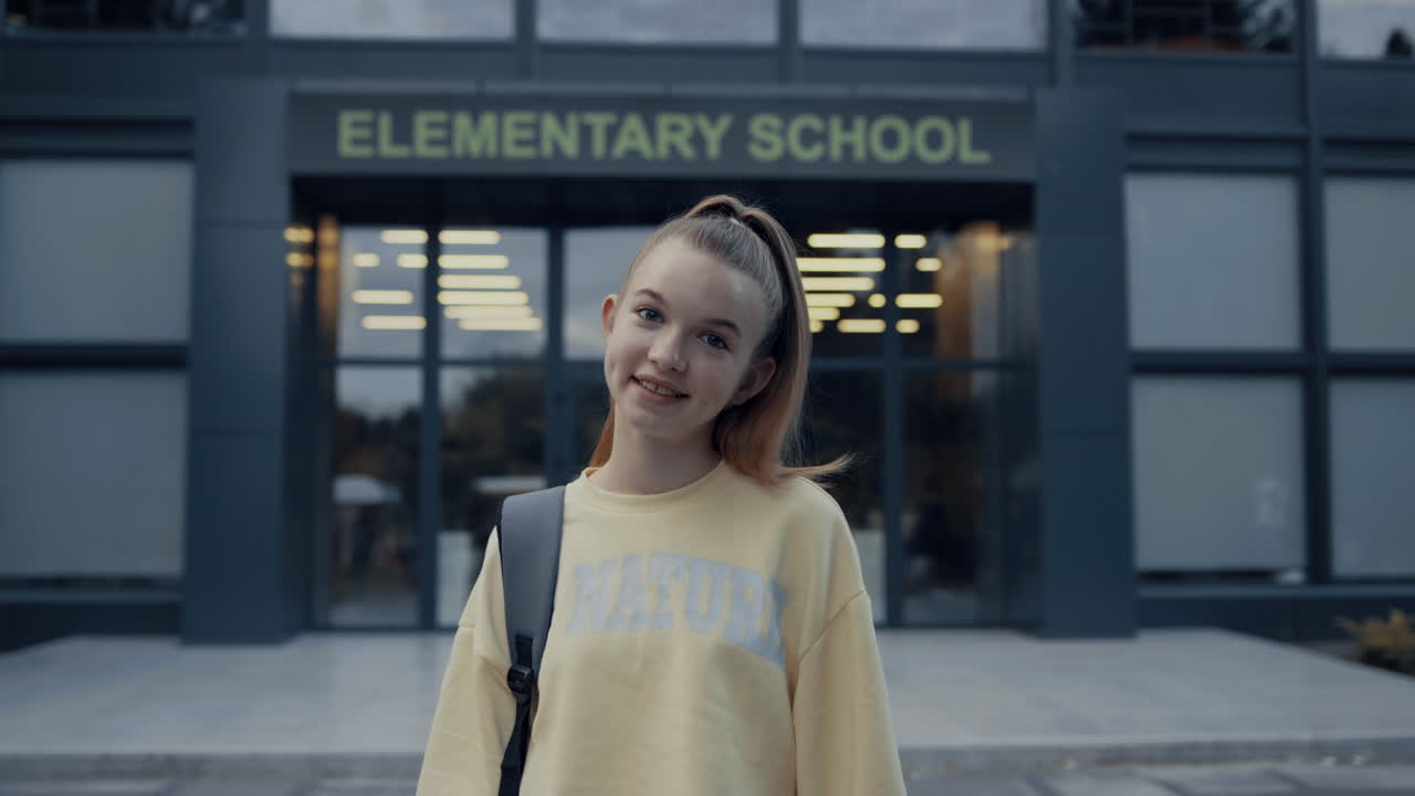 캠퍼스 입구에서 포즈를 취하는 십대 여학생. 카메라에 미소 짓는 아이.