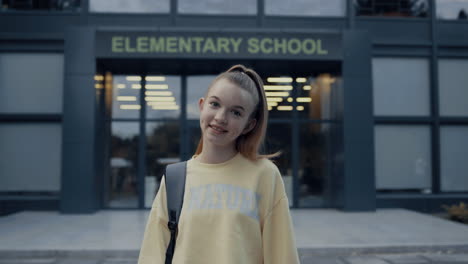 Teenage-school-girl-posing-at-campus-entrance-close-up.-Child-smiling-on-camera.