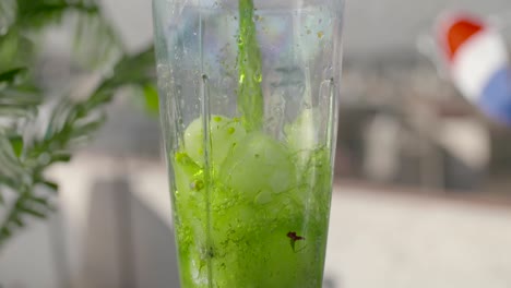 Pouring-Green-Juice-Inside-Blender-With-Ice-Cubes---close-up