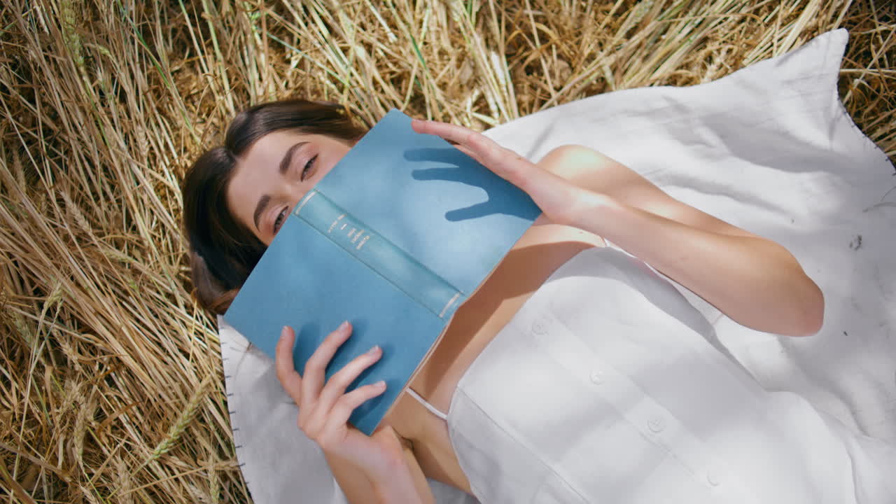 chica descansando escondiendo la cara con el libro textura de heno primer plano. ojos de la dama mirando la cámara