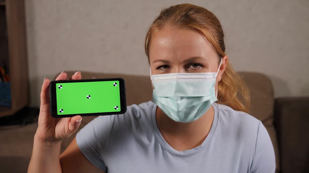 retrato de una mujer con una máscara con un teléfono en sus manos con una pantalla verde.