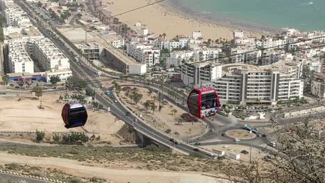 Cable-car-of-the-aerial-tramway-connecting-Oufella-peak-and-Agadir-city-in-Morocco,-overlooking-a-panoramic-view-of-the-beach