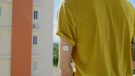 male checking his blood glucose levels on left arm with freestyle libre 2 sensor on hotel balcony