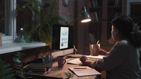 brunette woman sitting in front of computer while eating food and working