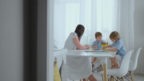 Mom-and-her-two-sons-sitting-at-the-kitchen-table-drawing-colored-pencils-family-drawing-on-the-lawn-in-the-summer.