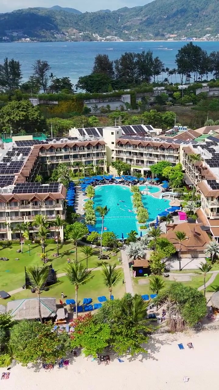 Tayland Phuket'teki lüks bir tatil köyünü sergileyen drone çekimi; havuzları, yemyeşil doğayı ve parlak gün ışığında sahil manzaralarını öne çıkarıyor.