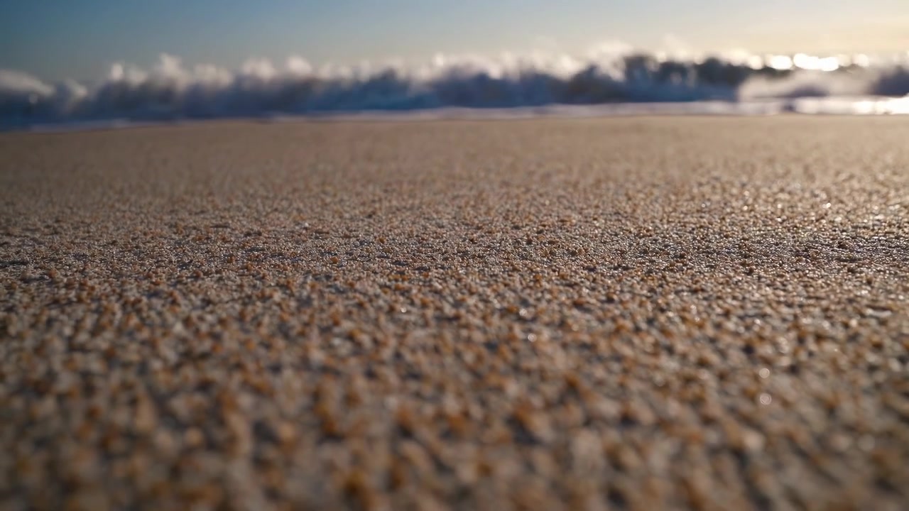 Nærbillede af sandstrand med havbølger der bruser i baggrunden