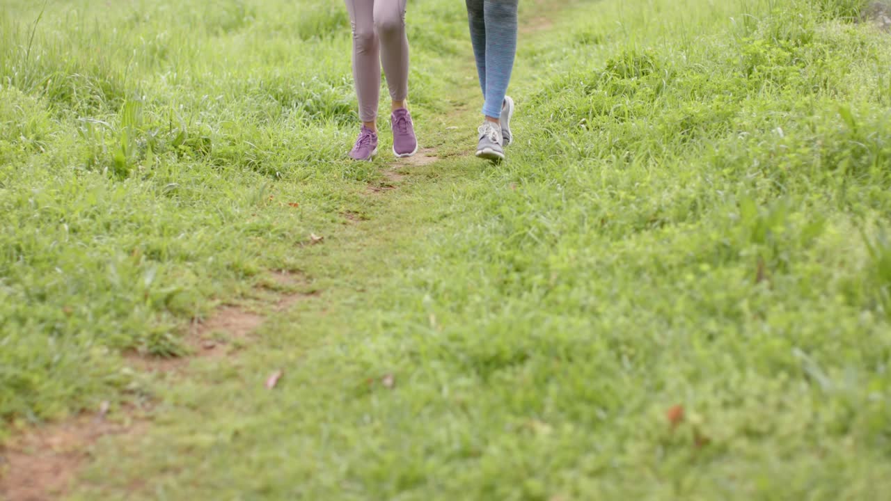 At start two women are jogging along grassy path, camera shifting torsos to shoes for fitness