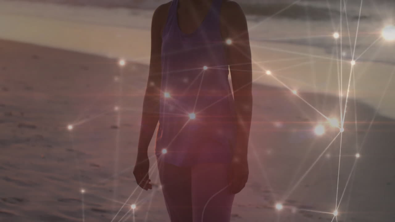 woman walking along sandy beach at dusk showcasing technology connection with glowing network nodes