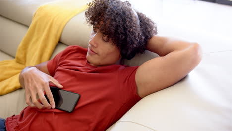 a young biracial man relaxes with headphones on sofa at home