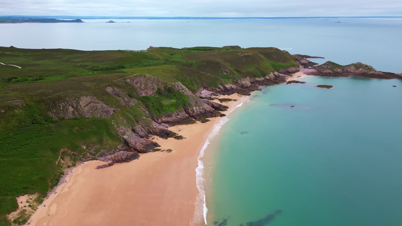 The idyllic Plage de Lourtuais beach, the rocky peninsula of Cap d'Erquy, and calm turquoise sea in Brittany, France. Aerial drone lateral