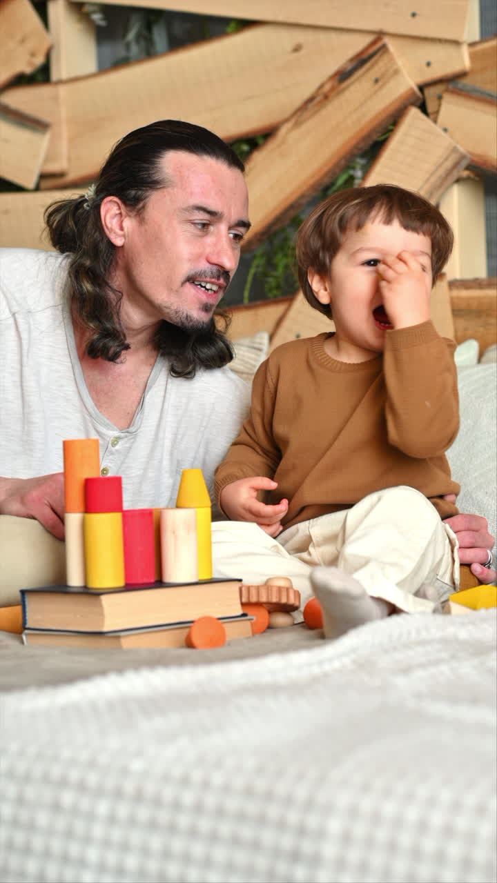 Father playing with his son with colourful, ecological wooden toys on the bed