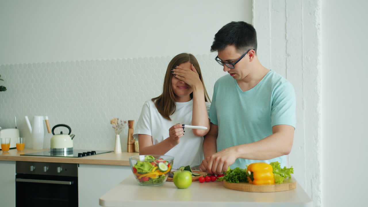 Couple reacts to pregnancy test results in the kitchen while preparing a salad