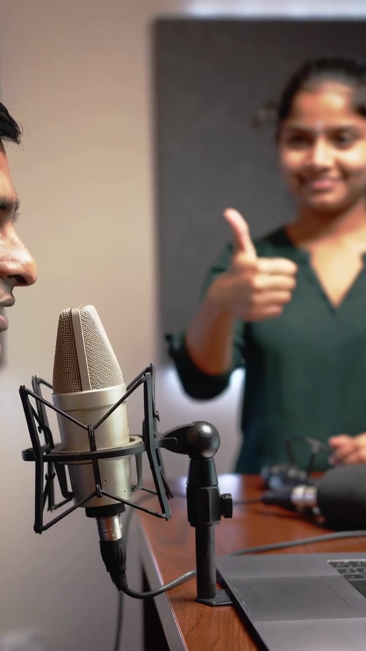Video vertical: Presentador en movimiento inclinándose hacia el micrófono en el estudio, copresentador con camiseta verde haciendo un pulgar hacia arriba, espacio para texto