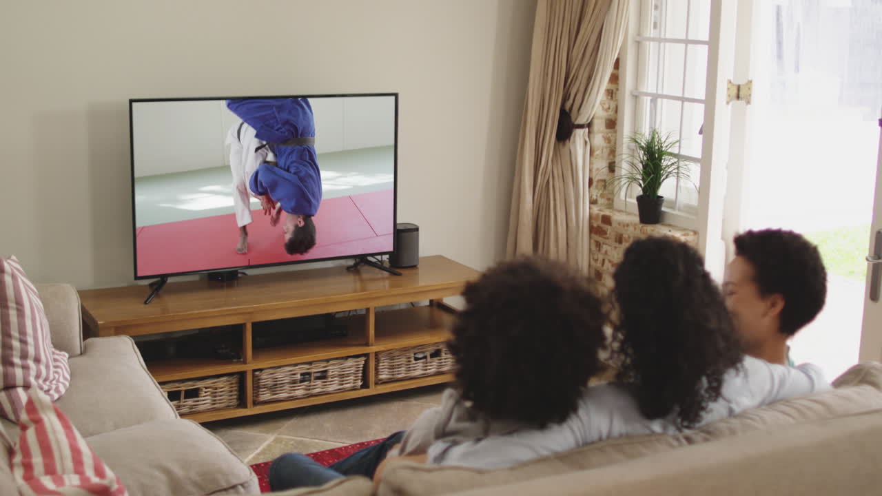 compuesto de una familia feliz sentada en casa juntos viendo un evento de partido de judo en la televisión