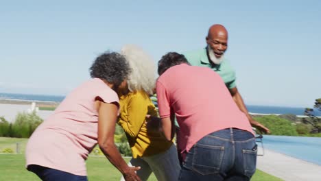 Happy-senior-diverse-people-playing-rugby-in-garden-at-retirement-home