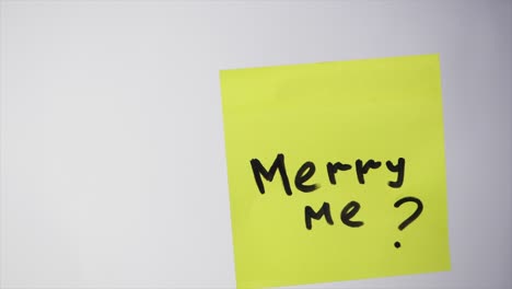 hand holding a yellow sticky note with the words merry me?