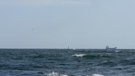 a lighthouse can be seen in the middle of the frame, next to it a cargo ship slowly passes by