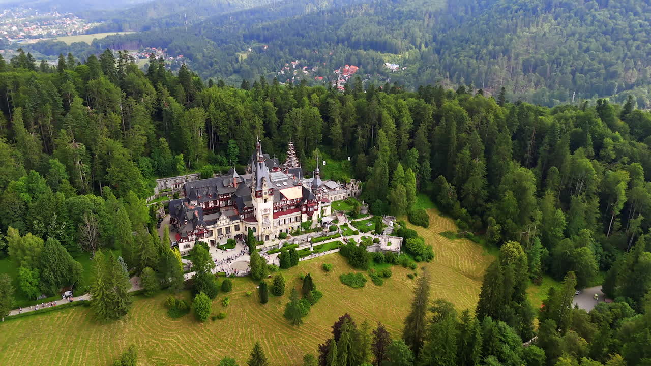 Gorgeous castle on the top of the mountain surrounded by the lush green pine tree wood. Aerial view on the Peles Castle in Prahova County, Romania