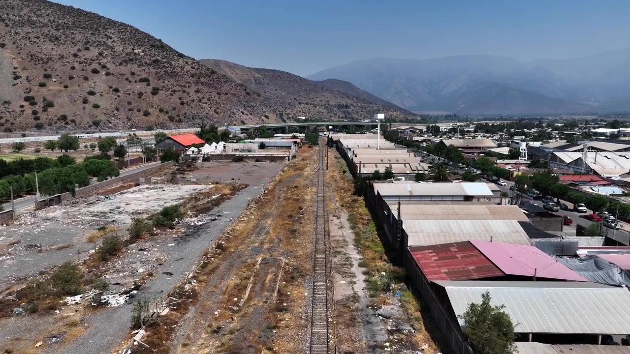 Vista aerea su un deposito ferroviario abbandonato con binari in disuso e lotti vuoti fiancheggiati da edifici industriali e pendii montuosi aridi nella valle dell'Aconcagua. Los Andes, Cile