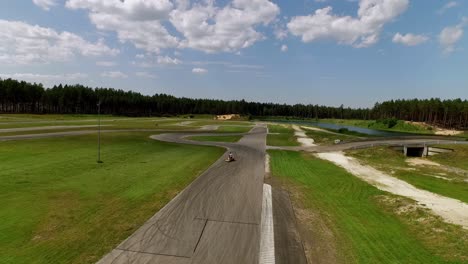 aerial panorama of latvia on a sunny summer day with fluffy white clouds, green grass, asphalt track, forest backdrop, blue sky, and distant buildings drone photography, wide angle lens