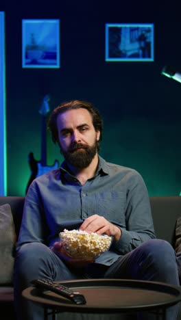vertical video sad man sitting on couch feeling heartbroken while watching tragic movie