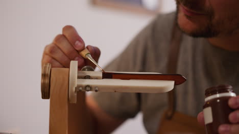 master applies paint on leather item fixed by clamp in shop