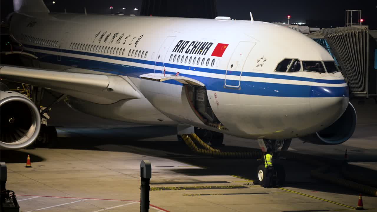 At night, an Air China plane is stationed on a runway at Beijing International Airport, China, with runway lights illuminating the aircraft and the surrounding airport facilities.