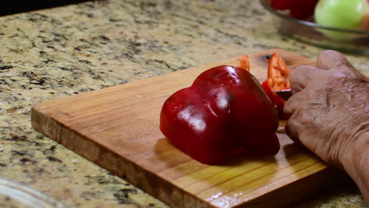 Close-up of a woman’s hands cutting a red bell pepper with a kitchen knife on a cutting board, showing fresh vegetable preparation