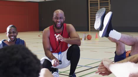 happy diverse male basketball team training with male coach in indoor court, in slow motion