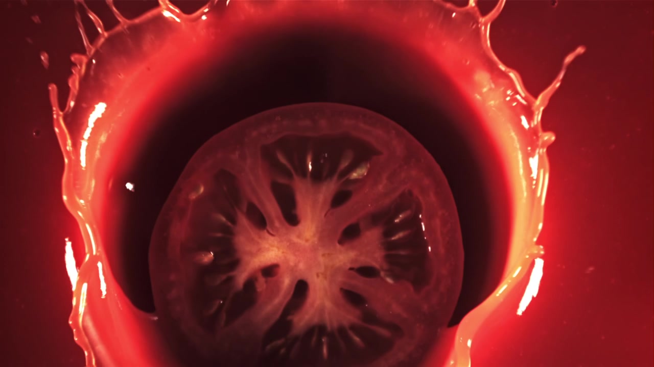 Fetta di pomodoro fresca che schizza in un liquido rosso al rallentatore.