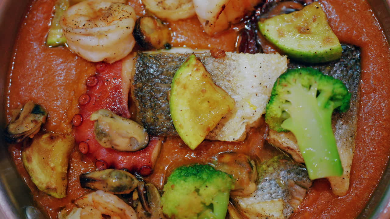 Primo piano di un piatto gourmet di frutti di mare in una salsa ricca con pesce, polpo, crostacei e verdure.