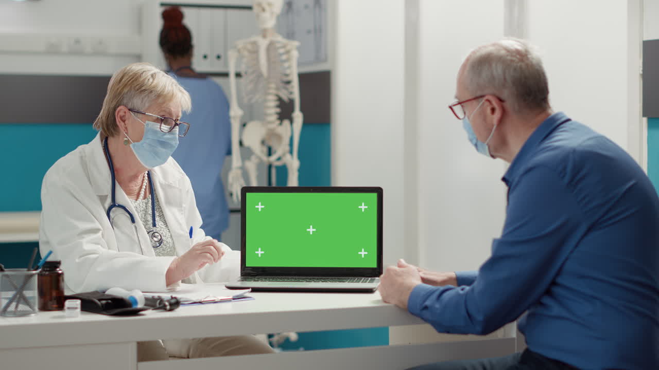 General practitioner showing laptop with greenscreen to retired patient