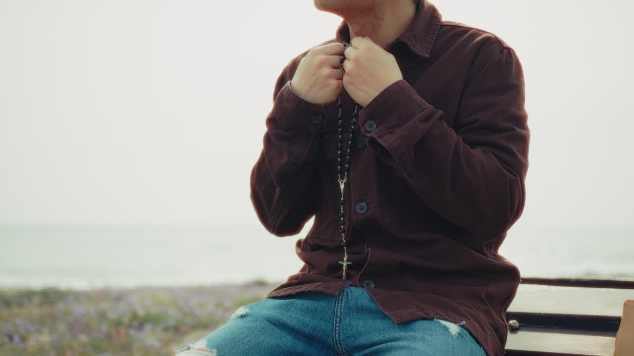 Man Holding A Rosary In His Hands During A Prayer On The Beach